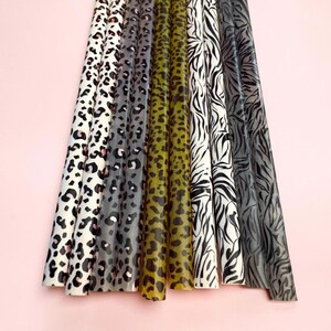 May include: A collection of eight long, cylindrical items arranged vertically. The patterns include white and black leopard print, grey and black leopard print, olive green and black leopard print, and black and white zebra stripes.
