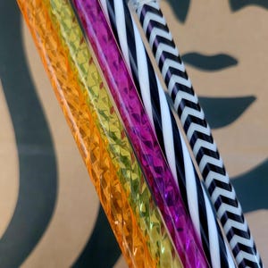Könnte beinhalten: Vier bunte Trinkhalme, darunter ein schwarz-weiß gestreifter Strohhalm, ein rosa-weiß gestreifter Strohhalm, ein gelb-grüner Spiralstrohhalm und ein orange-gelber Spiralstrohhalm.