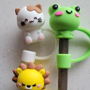 May include: Three colorful silicone straw toppers with animal faces. A white cat with brown ears, a green frog with pink cheeks, and a yellow lion with brown mane.