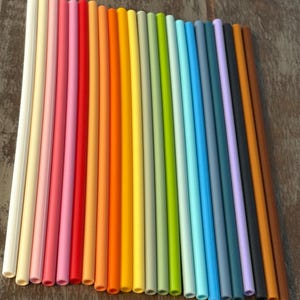 Può includere: Una collezione di cannucce riutilizzabili colorate, che vanno dal bianco al marrone, passando per il rosa, il rosso, l'arancione, il giallo, il verde e il blu. Le cannucce sono disposte in diagonale, mostrando un arcobaleno di colori.
