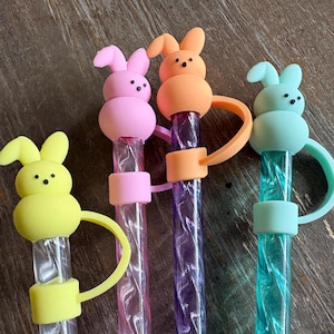 May include: Four colorful bunny-topped straws. The bunny heads are yellow, pink, orange, and blue. The straws are clear with colorful accents. The straws have a loop attached to the bunny head and the straw.