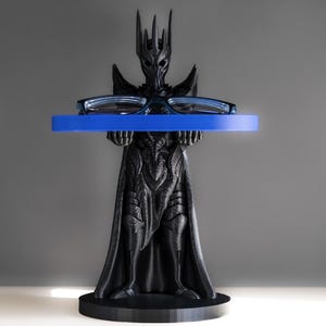 May include: A black plastic stand shaped like a fantasy character holding a blue tray. The tray is designed to hold glasses or other small items.
