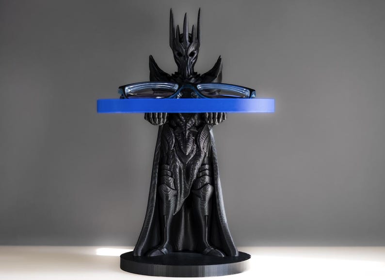 May include: A black plastic stand shaped like a fantasy character holding a blue tray. The tray is designed to hold glasses or other small items.