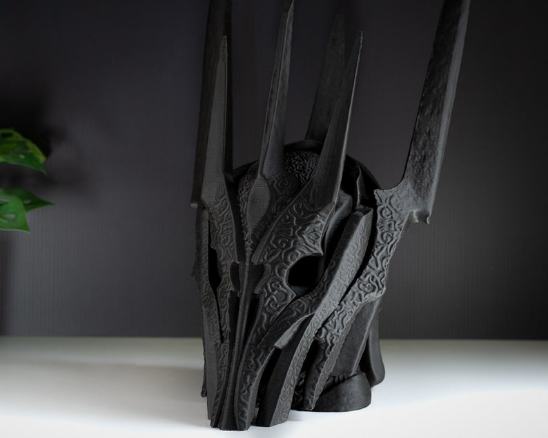 May include: A black, detailed, 3D printed helmet with a crown of spikes. The helmet is made of a textured material and has a detailed design.