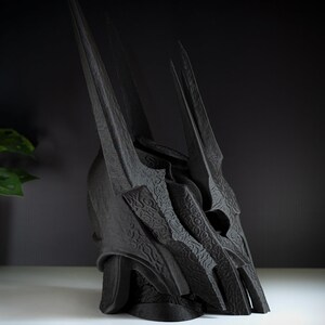 May include: A black 3D printed crown with a detailed, textured design. The crown has a tall, pointed shape with multiple spikes.