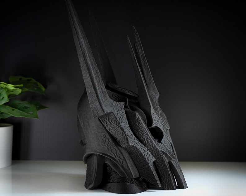 May include: A black 3D printed crown with a detailed, textured design. The crown has a tall, pointed shape with multiple spikes.
