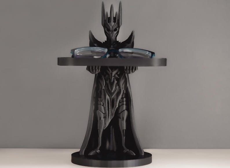 May include: Black 3D printed figurine of a dark lord holding a tray for glasses. The figurine is wearing a crown and a long robe.