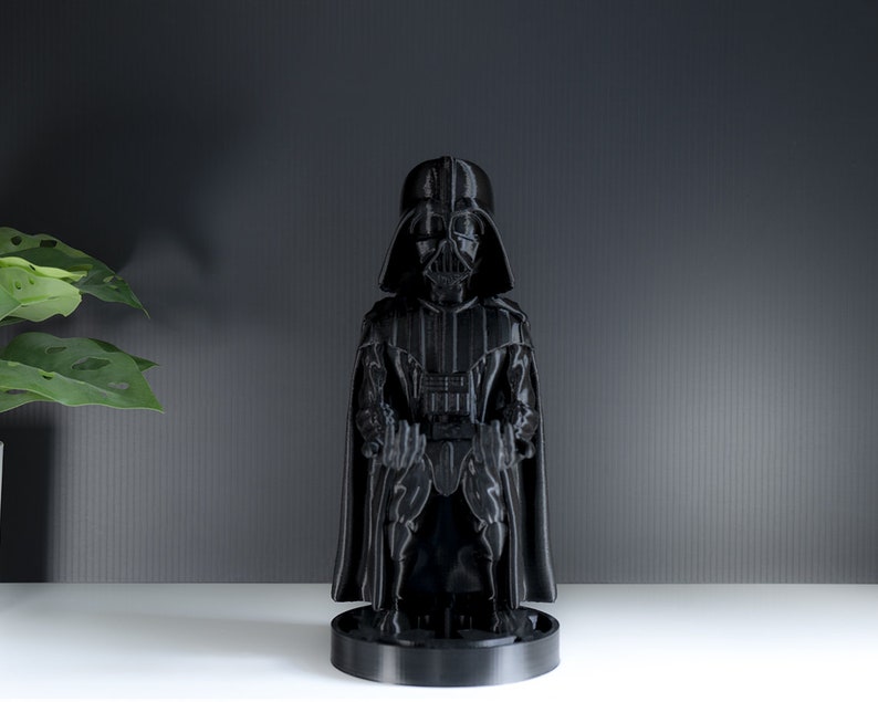 May include: A black Darth Vader figurine with a cape and a black base. The figurine is standing on a white surface.