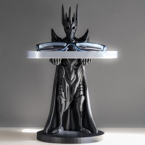 May include: A black 3D printed figurine of a dark lord holding a tray with a pair of glasses on it. The figurine is wearing a crown and a long robe.