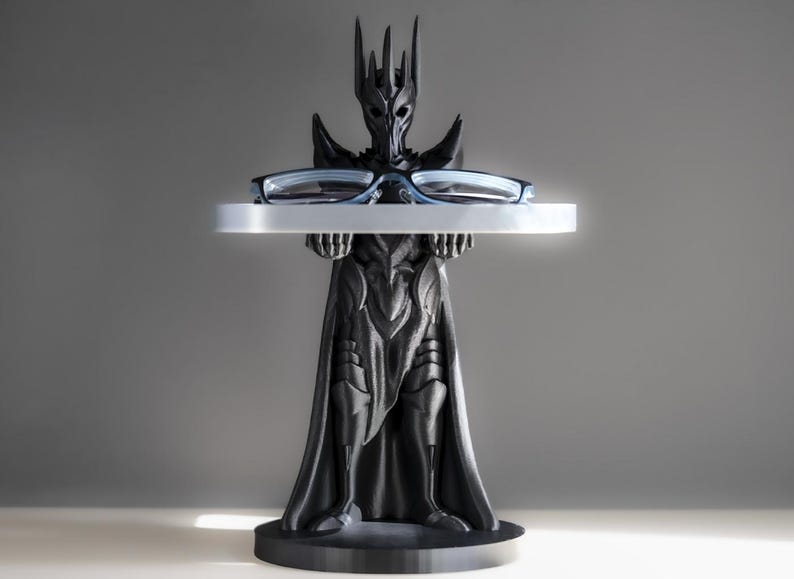 May include: A black 3D printed figurine of a dark lord holding a tray with a pair of glasses on it. The figurine is wearing a crown and a long robe.