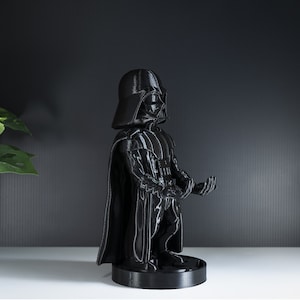 May include: A black Darth Vader figurine with a cape and a lightsaber. The figurine is standing on a black base.