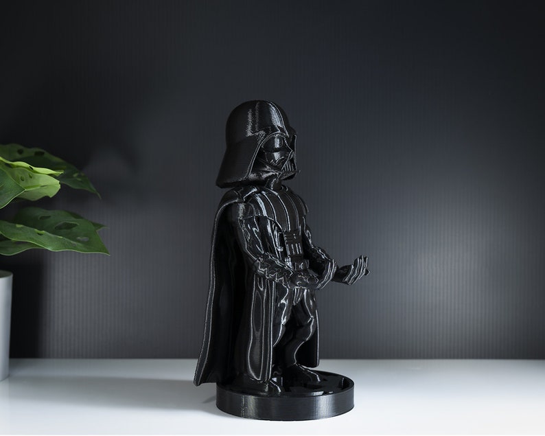 May include: A black Darth Vader figurine with a cape and a lightsaber. The figurine is standing on a black base.