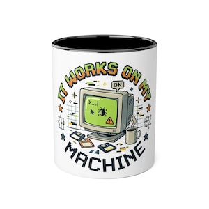 May include: A white ceramic mug with a black interior featuring a pixel art graphic of a vintage computer monitor displaying a bug icon and a warning symbol. The text reads IT WORKS ON MY MACHINE, accompanied by floppy disks and a coffee mug.