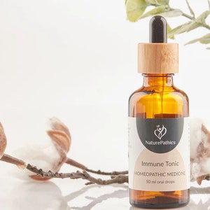 May include: An amber glass bottle with a wooden cap and dropper, labelled "Immune Tonic" with "NaturePathics" branding. The bottle contains 50 ml of homeopathic medicine. Cotton branches and a potted plant are in the background.