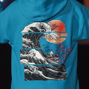 May include: A turquoise hoodie featuring a graphic of a large wave, a red sun, and a mountain. The wave design is in black and white, with a blue background. Red flowers are on the right side of the design.