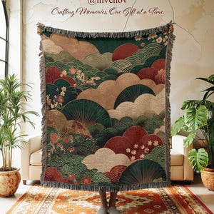 May include: A woven blanket with a Japanese-inspired design featuring stylized clouds, fans, and floral elements in shades of green, red, and beige. The blanket has a fringed edge and the text "@invenov Crafting Memories, One Gift at a Time."