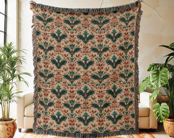 May include: A beige throw blanket with a repeating pattern of teal and burgundy floral designs. The blanket has a fringed edge and is held up in front of a person. The text "@invenov Crafting Memories, One Gift at a Time." is visible in the background.