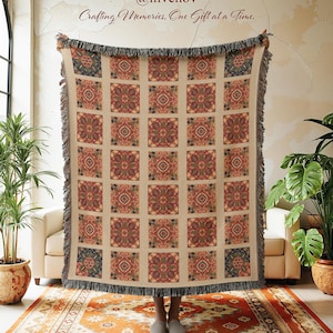May include: A beige throw blanket with a repeating square pattern in red, green, and blue. The blanket has a fringed edge and is held up in front of a person. The text "@invenov Crafting Memories, One Gift at a Time." is in the upper right corner.