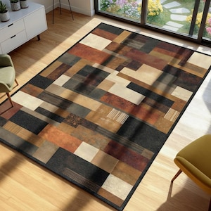 May include: A rectangular area rug with a geometric pattern in shades of brown, beige, and black. The rug features a patchwork design with rectangular and linear shapes. The rug is placed on a hardwood floor.