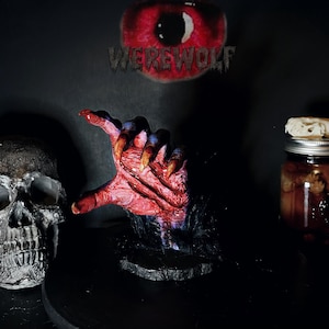 May include: A Halloween-themed display featuring a red, clawed hand emerging from black fur. A skull and a jar with a bone are also visible. The word "WEREWOLF" is above the hand, with a red eye in the background.
