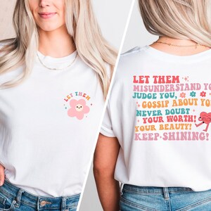 May include: White t-shirt with a pink flower graphic and the text "Let them" on the front. The back of the shirt has the text "Let them misunderstand you, judge you, gossip about you, never doubt your worth! Your beauty! Keep shining!" with a pink heart graphic.