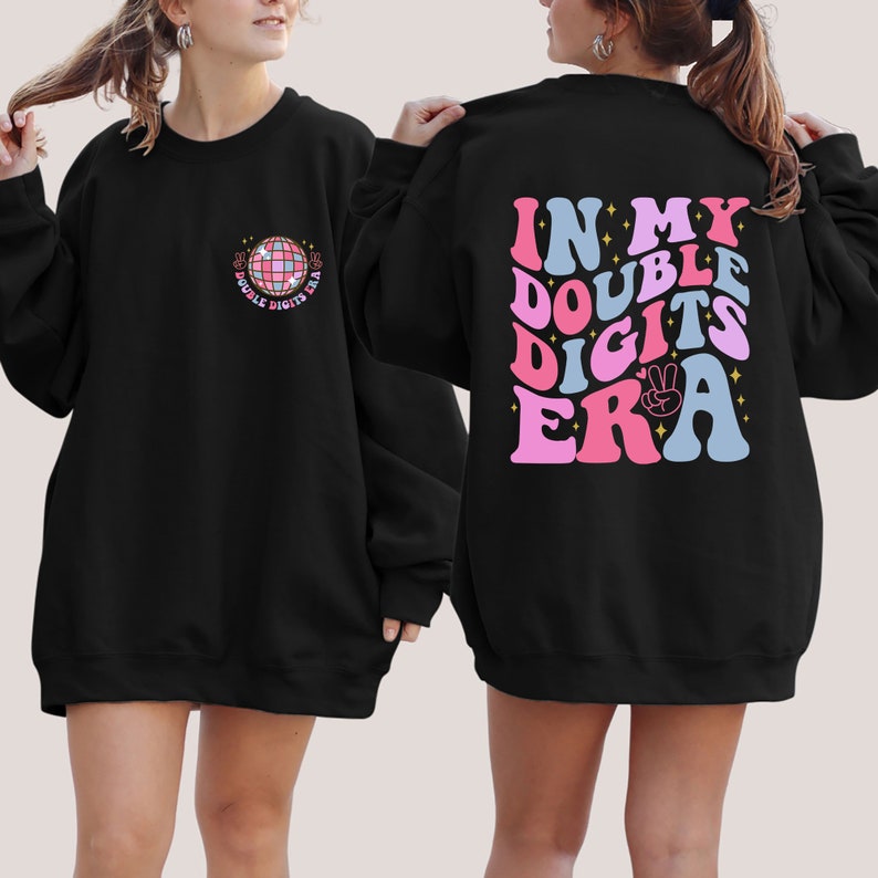 May include: Black sweatshirt with a retro-style graphic on the back that says "In My Double Digits Era" with a peace sign. The front of the sweatshirt has a small graphic of a disco ball with the text "Double Digits Era".