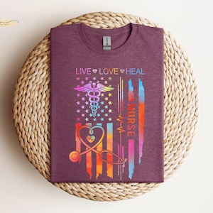 May include: A maroon t-shirt with a colorful American flag design. The flag has a medical caduceus symbol and the words "Live Love Heal Nurse".