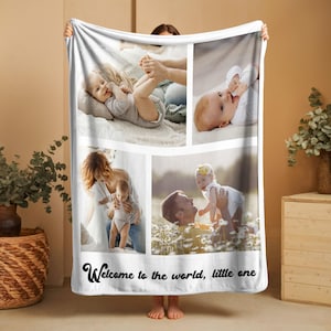 May include: White fleece blanket featuring four photo panels of a baby with family. The blanket has the text "Welcome to the world, little one" in a script font at the bottom. The photos show the baby in different settings.