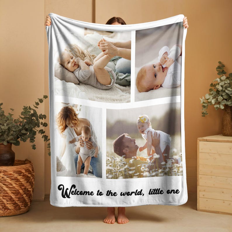 May include: White fleece blanket featuring four photo panels of a baby with family. The blanket has the text "Welcome to the world, little one" in a script font at the bottom. The photos show the baby in different settings.
