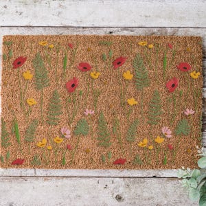 May include: Rectangular doormat with a floral design. The mat features a brown background with a pattern of red poppies, yellow flowers, green ferns, and pink blossoms. The design is printed on a textured surface.