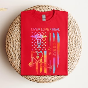 May include: Red t-shirt with a rainbow-colored American flag design. The flag features a medical caduceus symbol and the text "LIVE LOVE HEAL NURSE".