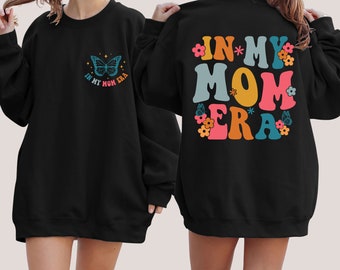 May include: Black sweatshirt with a butterfly graphic and the text "In My Mom Era" on the front and the text "In My Mom Era" in colorful letters with flowers on the back.