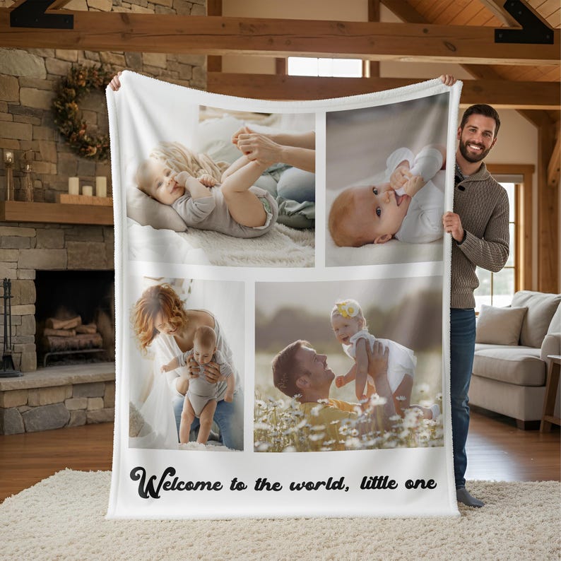 May include: A white fleece blanket featuring four photo panels of a baby with parents. The blanket has the text "Welcome to the world, little one" in a black script font. The blanket is held up by a person.