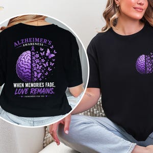 May include: A black t-shirt featuring a graphic of a purple brain transitioning into butterflies. The back design includes the text ALZHEIMER'S AWARENESS, WHEN MEMORIES FADE, LOVE REMAINS, and I REMEMBER FOR YOU. The front chest area displays a smaller version.