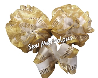 May include: Three large, decorative hair bows in white and gold. The bows feature layers of ruffled ribbon with a gold chevron pattern and gold glitter edges. The text "Sew Marvelous" is visible on the bottom left of the image.