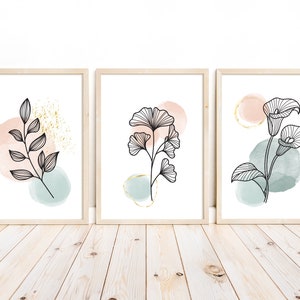 Può includere: Tre stampe artistiche botaniche incorniciate. Ogni stampa presenta un disegno a tratto nero di una pianta su uno sfondo acquerellato rosa, blu e oro. Le cornici sono in legno chiaro.