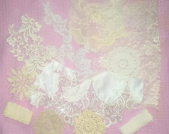May include: An assortment of delicate lace and fabric pieces in shades of white and cream, arranged on a pink surface. The collection includes various lace trims, doilies, and sections of fabric with floral and ornate patterns, ideal for crafting or embellishment.