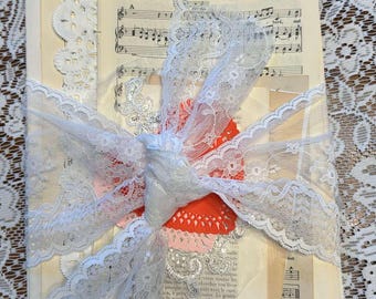 May include: A stack of vintage paper with lace and a red heart. The paper has music notes and text printed on it.