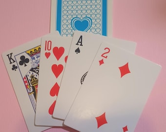 May include: Five playing cards on a pink background. The cards are a King of Clubs, a 10 of Hearts, an Ace of Spades, a 2 of Diamonds, and another 2 of Diamonds.