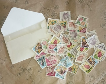 May include: A white envelope with a stack of vintage postage stamps featuring various designs, including birds, flowers, and seashells. The stamps are in shades of blue, red, green, and brown.