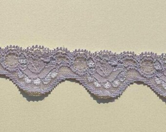 May include: A length of lavender lace with a scalloped edge. The lace features a delicate floral pattern and a semi-sheer design. The lace is suitable for various craft and sewing projects.
