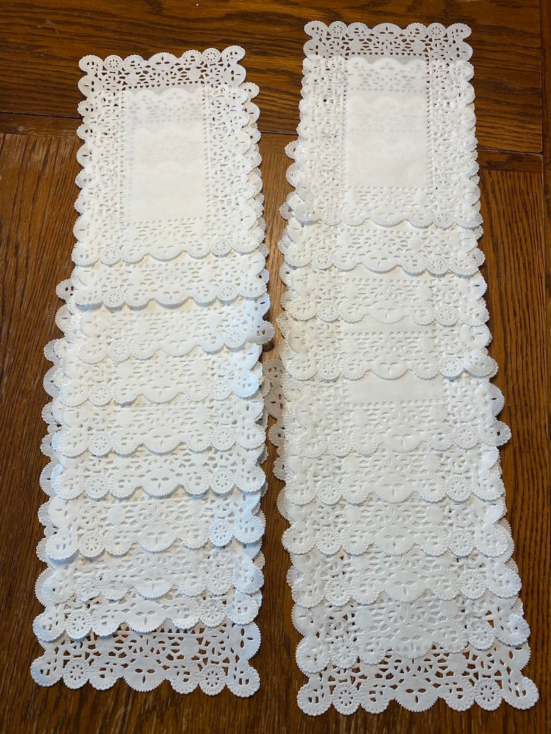 May include: Two stacks of white paper doilies with a delicate lace pattern. Each stack contains 10 doilies.