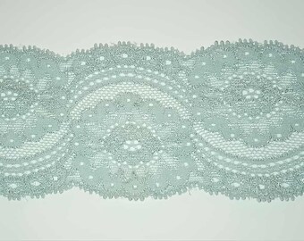May include: A length of pale teal lace with a repeating floral pattern. The lace features a scalloped edge and intricate openwork details. The delicate design is suitable for various craft projects.
