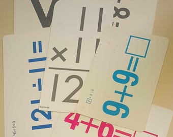 May include: A set of white flashcards with math problems written in black, blue, and pink. The problems include addition, subtraction, multiplication, and division. The flashcards are used for teaching basic math skills.