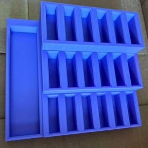 May include: A stackable, lavender-colored organizer with multiple rectangular compartments. The organizer features a tray on the side and is designed to hold small items. The design is simple and functional, suitable for various organizational needs.
