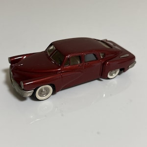 Könnte beinhalten: Ein Modellauto in Burgunderrot mit Weißwandreifen. Das klassische Fahrzeug hat ein stromlinienförmiges Design, Chromakzente und einen detaillierten Innenraum. Das Auto ist eine Miniaturreplik eines Oldtimers.