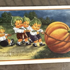 Może przedstawiać: Vintage pocztówka na Halloween przedstawiająca czwórkę kreskówkowych dzieci ciągnących dużą pomarańczową dynię za pomocą liny. Dzieci mają na sobie białe koszule, szorty i kapelusze w kształcie liści. Tekst na dole brzmi: "There'll be no fun tonight Without a Jack o'lantern light."