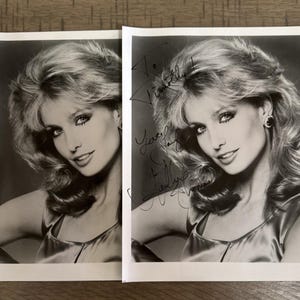 May include: Two black and white photographs of a woman with blonde hair, wearing a satin top and earrings. One photo has handwritten text. The woman is smiling and looking towards the camera.