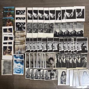 Puede incluir: Una colección de fotografías e impresiones en blanco y negro. Las imágenes incluyen retratos, paisajes y diseños gráficos. Algunas impresiones presentan el texto "PUBLIC ENEMY" y "FEAR OF A BLACK PLANET".