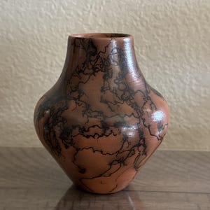 Puede incluir: Un jarrón hecho a mano, de color terracota, con una forma orgánica única. El jarrón presenta intrincados patrones negros en forma de relámpago en su superficie, agregando un contraste llamativo a los tonos cálidos y terrosos. Ideal para la decoración del hogar.